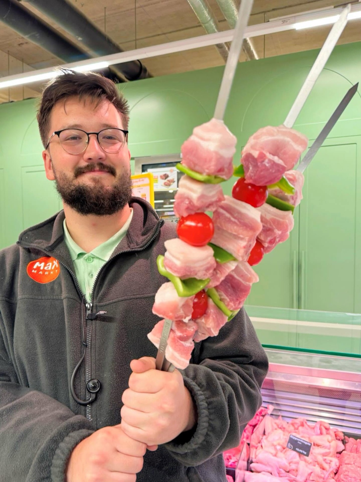 Een collega houdt drie spiesen shashlik met varkensvlees, paprika en tomaat omhoog bij de slagerij.