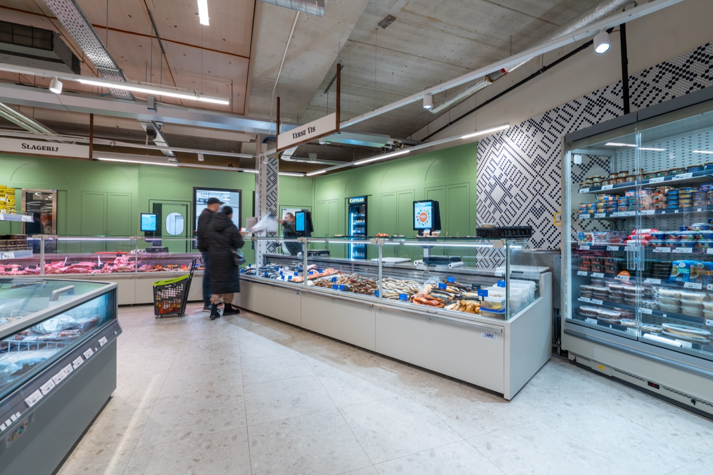 De toonbanken van de slagerij en de visafdeling tegen de groene wand, met het bord Verse Vis en de vyshyvanka-kolom ernaast.
