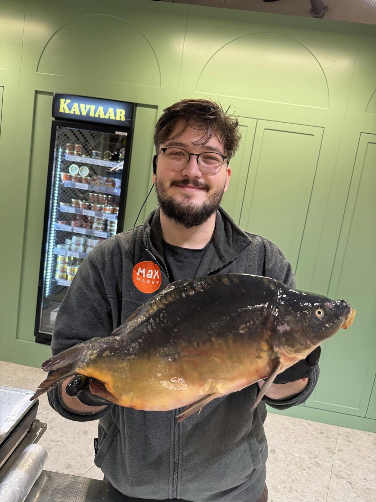 Onze visman houdt met beide handen een grote verse karper vast, voor de koelkast met kaviaar.