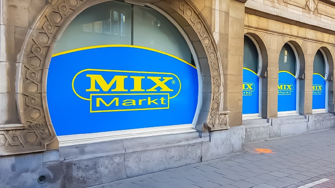 De winkel in Antwerpen Centrum achter een rij gebeeldhouwde stenen bogen, met in elk raam het blauwgele Mix Markt-logo.