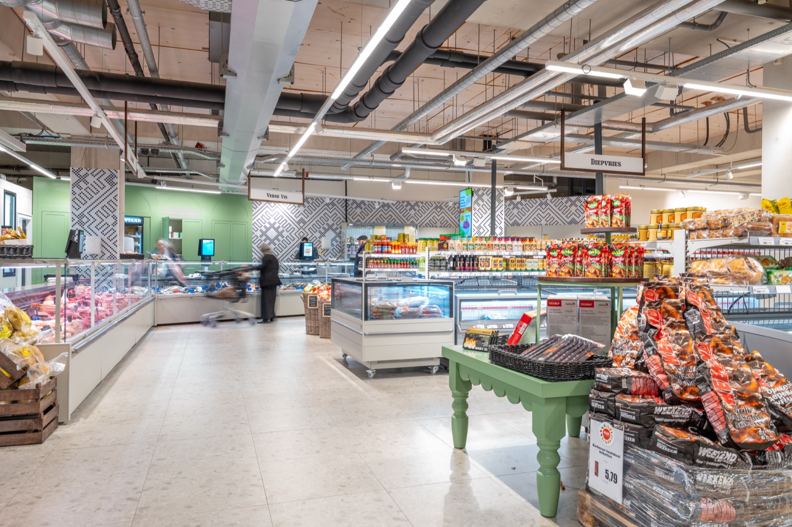 Blik door de winkel in Tilburg: de verse toonbanken van slagerij en vis links, het bord Verse Vis boven de balie en rechts de schappen met kruidenierswaren.